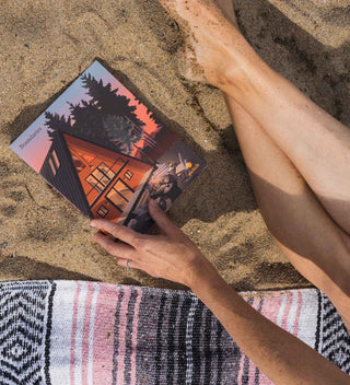 Person holding a deck of cards on a sandy beach with a towel underneath