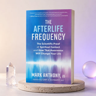 The Afterlife Frequency book by Mark Anthony, JD, standing upright on a round stone coaster. The book cover features a blue-to-purple gradient with white text and a glowing wave-like pattern near the bottom.