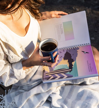 Person holding a mug with a scenic notebook open on their lap