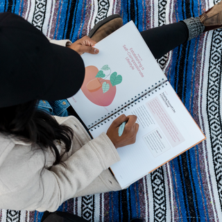 Person reading a book with a colorful illustration on a patterned rug