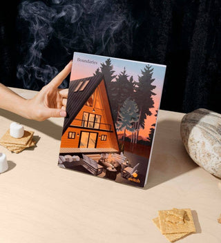 Hand holding a journal titled 'Boundaries' with a cabin illustration on a table.