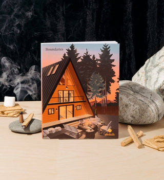 Journal with a cabin illustration on a wooden surface with rocks and candles.