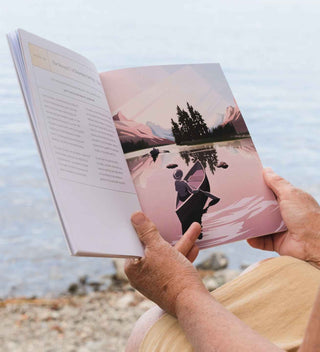 Person reading a book with a scenic cover by a lake