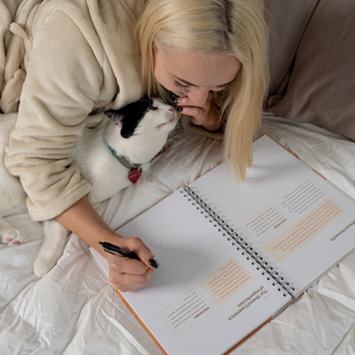 Woman lying on a bed with a cat, writing in a notebook